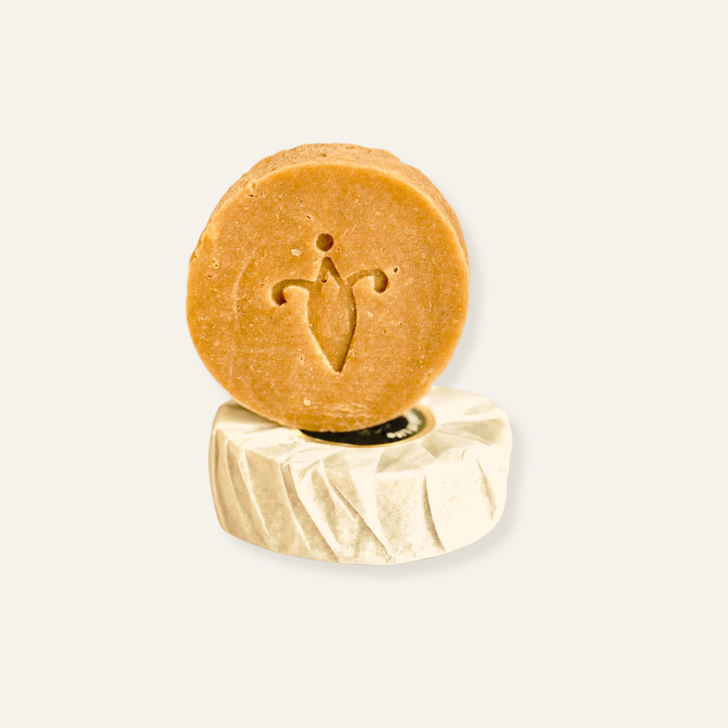 Round brown soap bar with a logo on  a wrapped soap stand against a light gray background