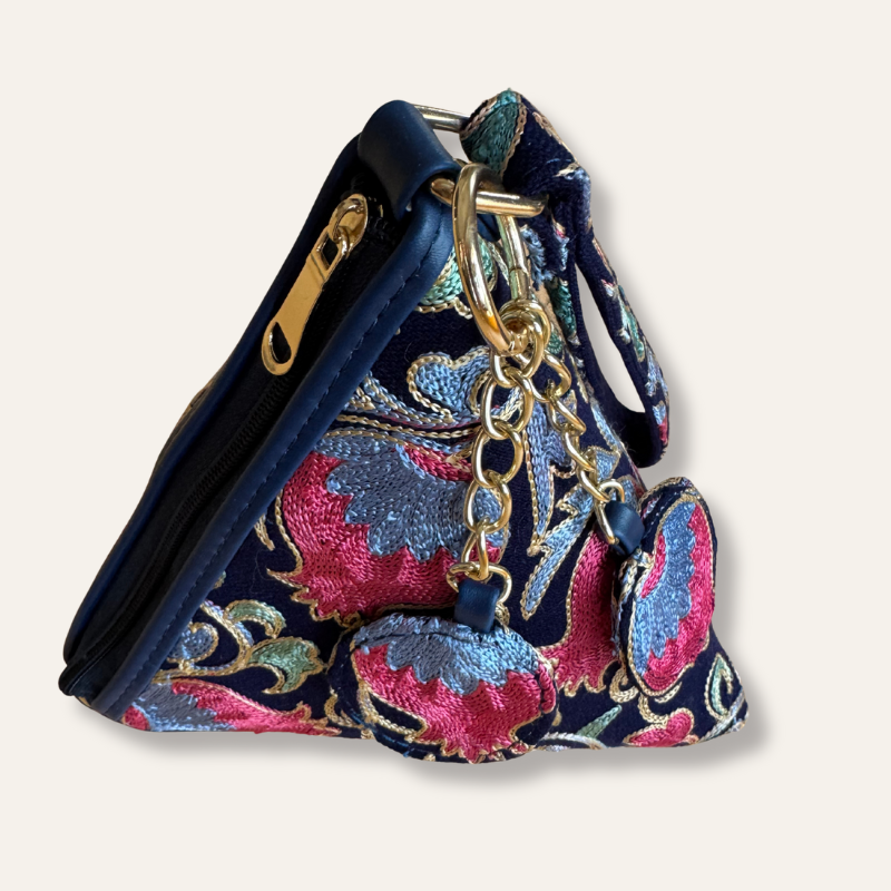 Navy blue bag with pink and gold floral embroidery and keychain on a light gray background