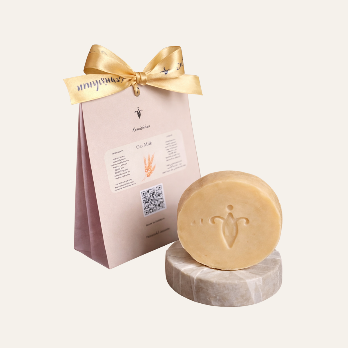 Bar of oat soap on a marble stand with a branded pink packaging sleeve and gold ribbon.
